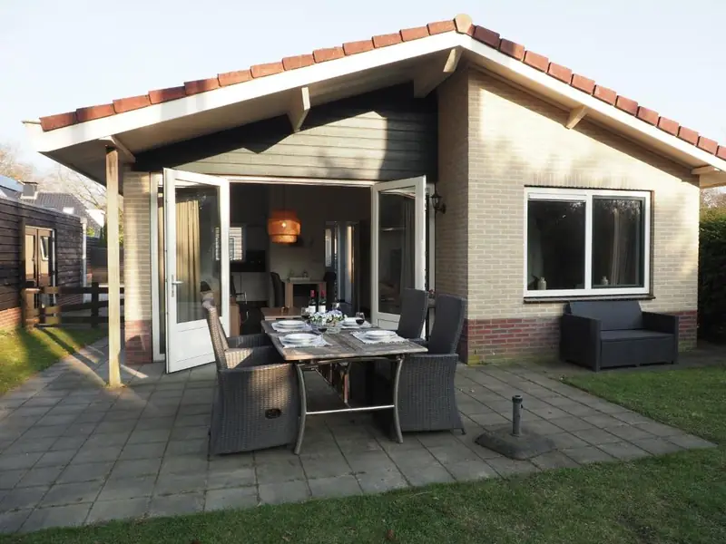 De gedekte tafel op het terras van huisje&nbsp;3, voor de openslaande deuren aan de achterkant, met binnen de rotan hanglamp.