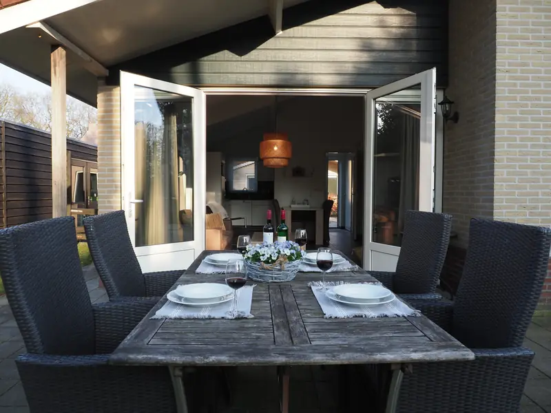 Die Terrasse von Haus&nbsp;3: der gedeckte Tisch vor den offenen Flügeltüren, drinnen die Rattanleuchte.